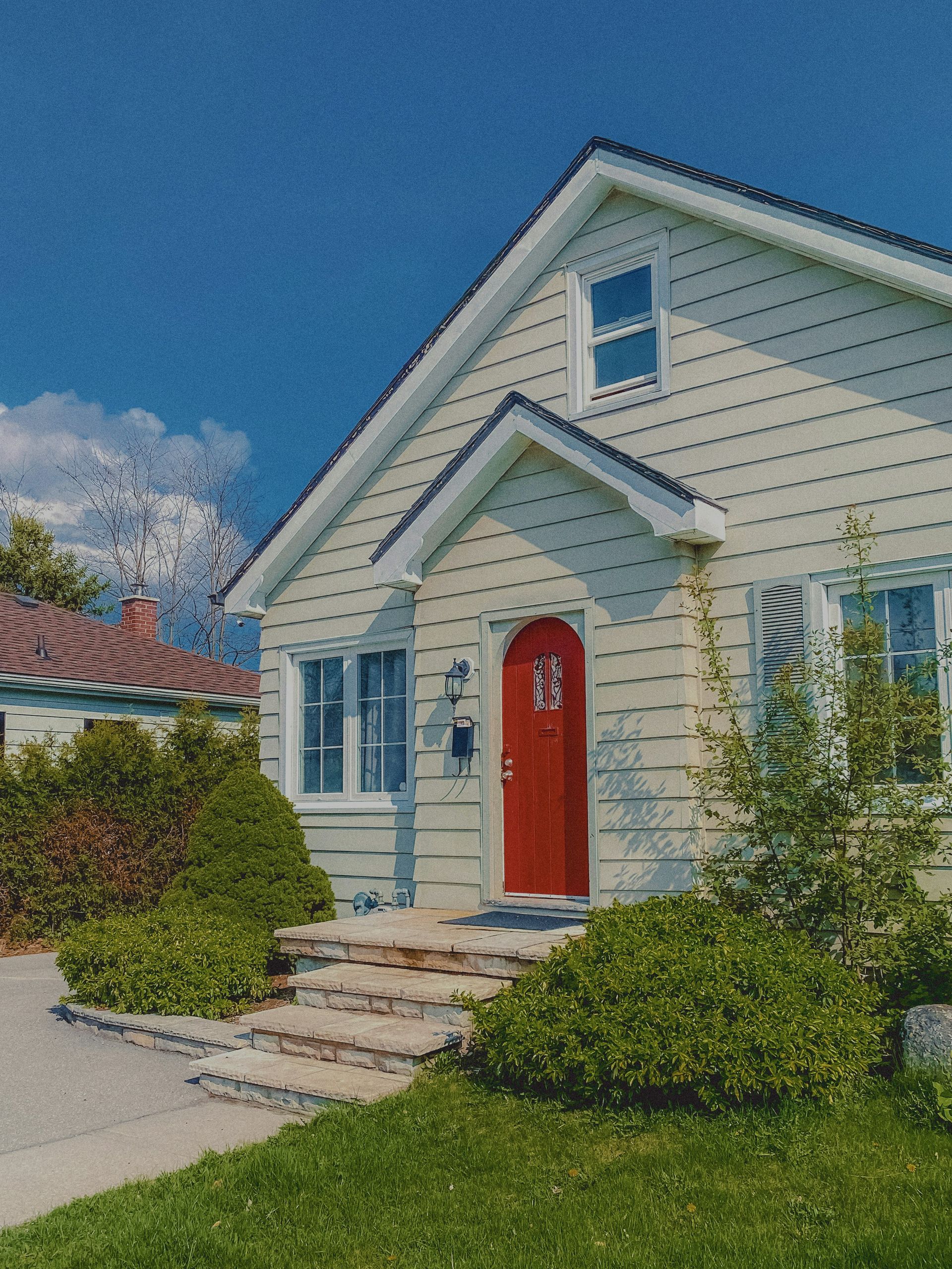 Cozy house with red door under a blue sky.